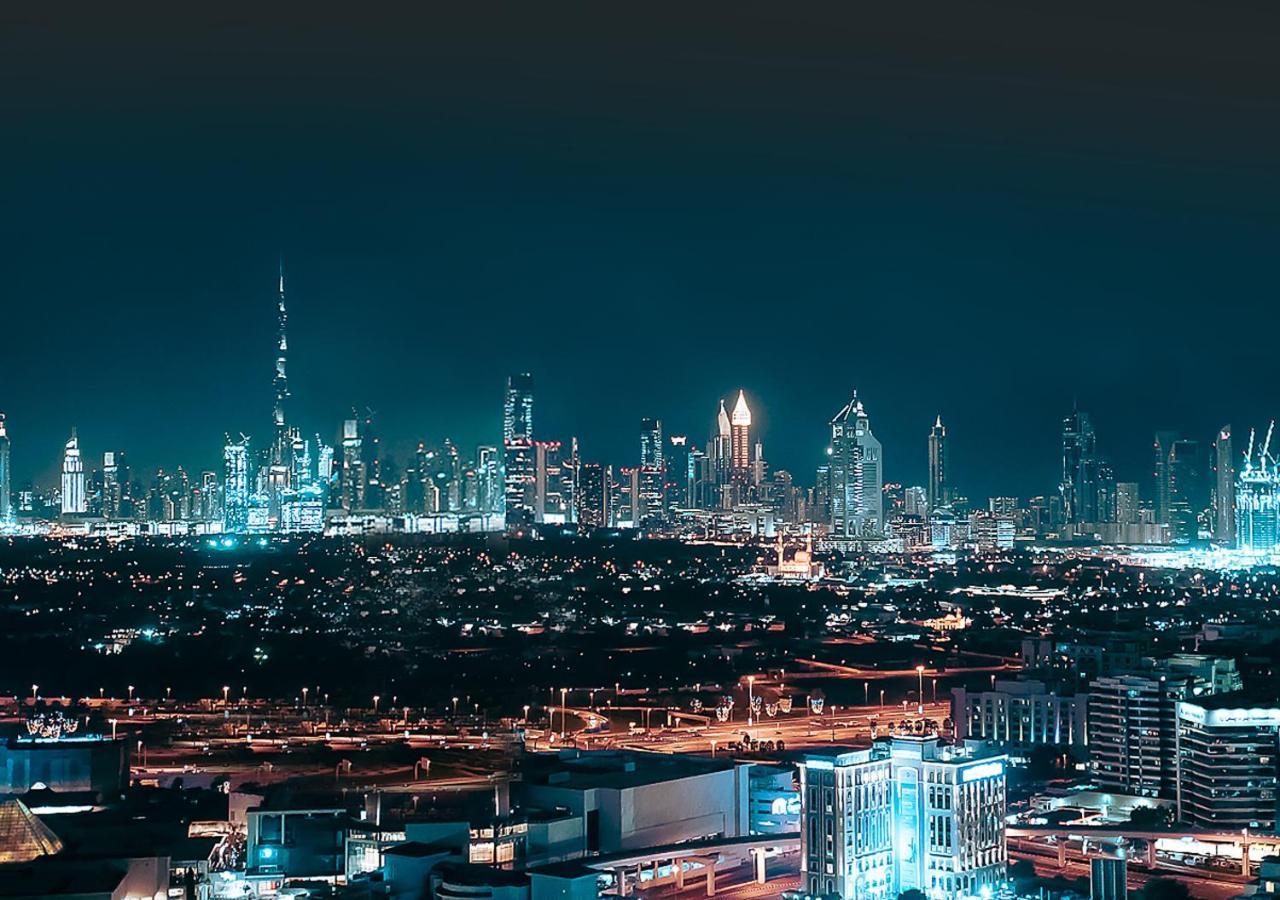 Hyatt Regency Dubai Creek Heights Hotel Exterior photo The photo depicts a vibrant urban skyline at night. Tall skyscrapers dominate the scene, showcasing modern architecture and illuminated buildings. One of the most prominent structures is a very tall tower, identifiable by its unique design and bright