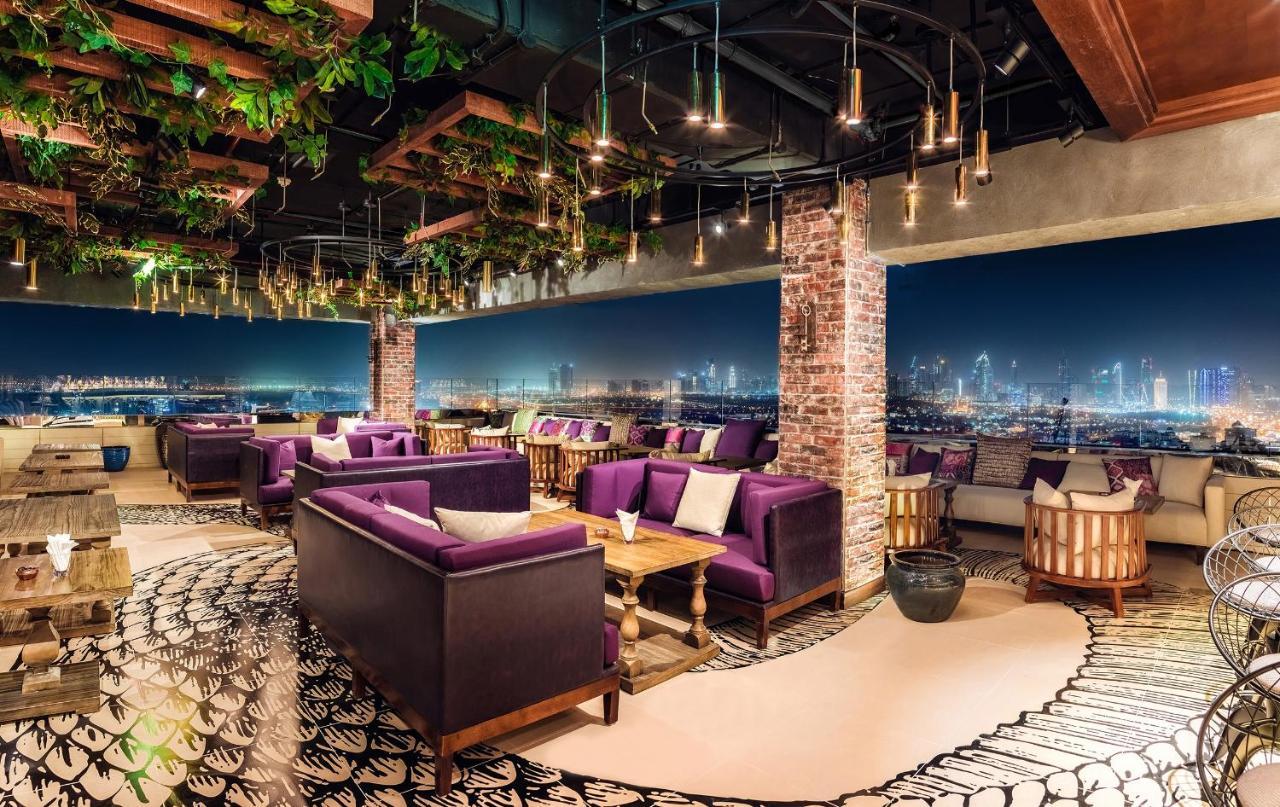 Hyatt Regency Dubai Creek Heights Hotel Exterior photo The photo depicts a stylish and modern lounge or restaurant interior. It features plush purple sofas arranged around wooden tables, creating a cozy and inviting atmosphere. The space is adorned with abundant greenery, adding a touch of nature to the 