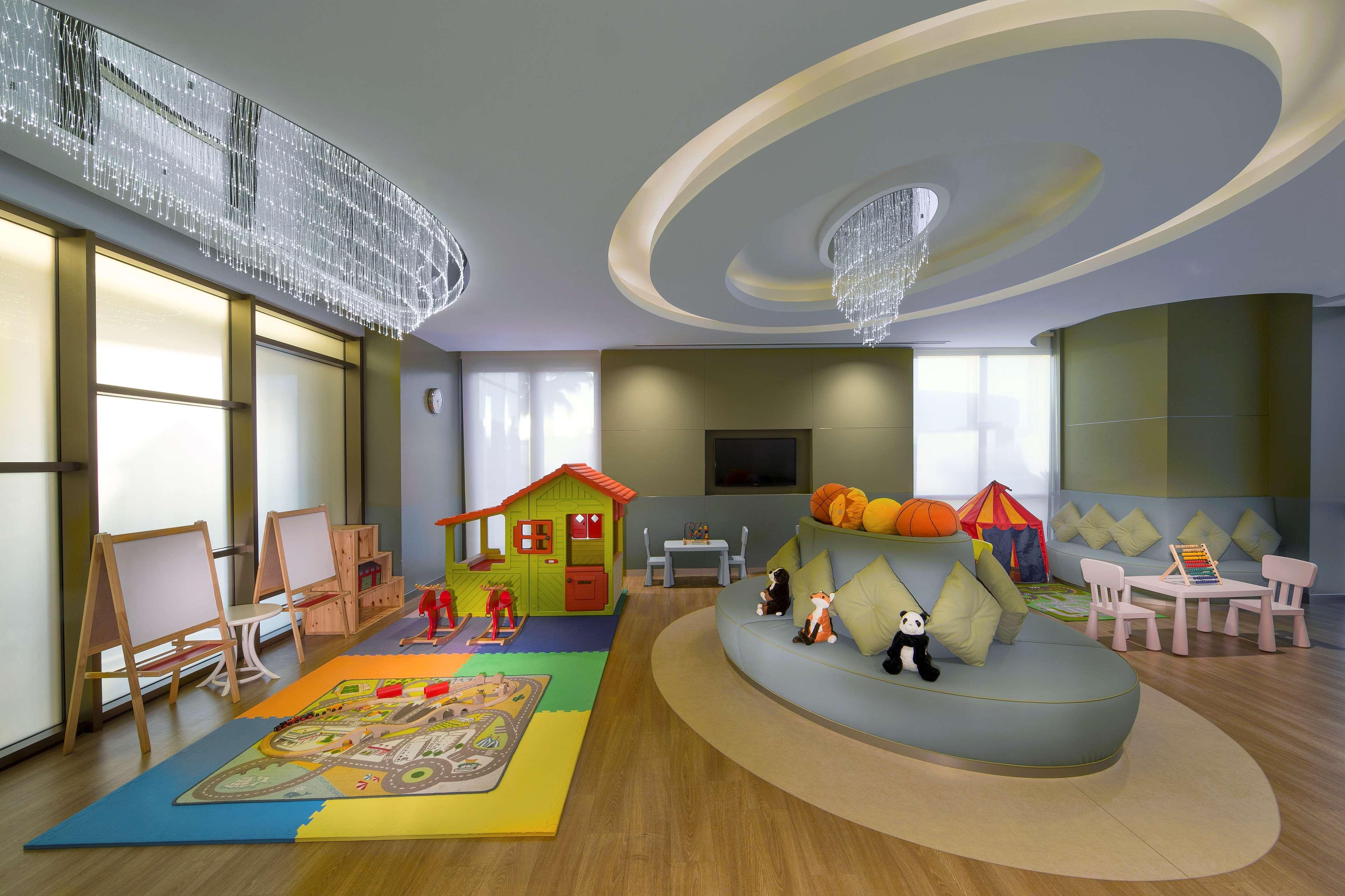 Hyatt Regency Dubai Creek Heights Hotel Exterior photo The photo depicts a brightly colored children's playroom. It features a variety of engaging play areas, including a small playhouse, a soft play surface with a large game mat, and a cozy seating area with plush toys. There are several educational and