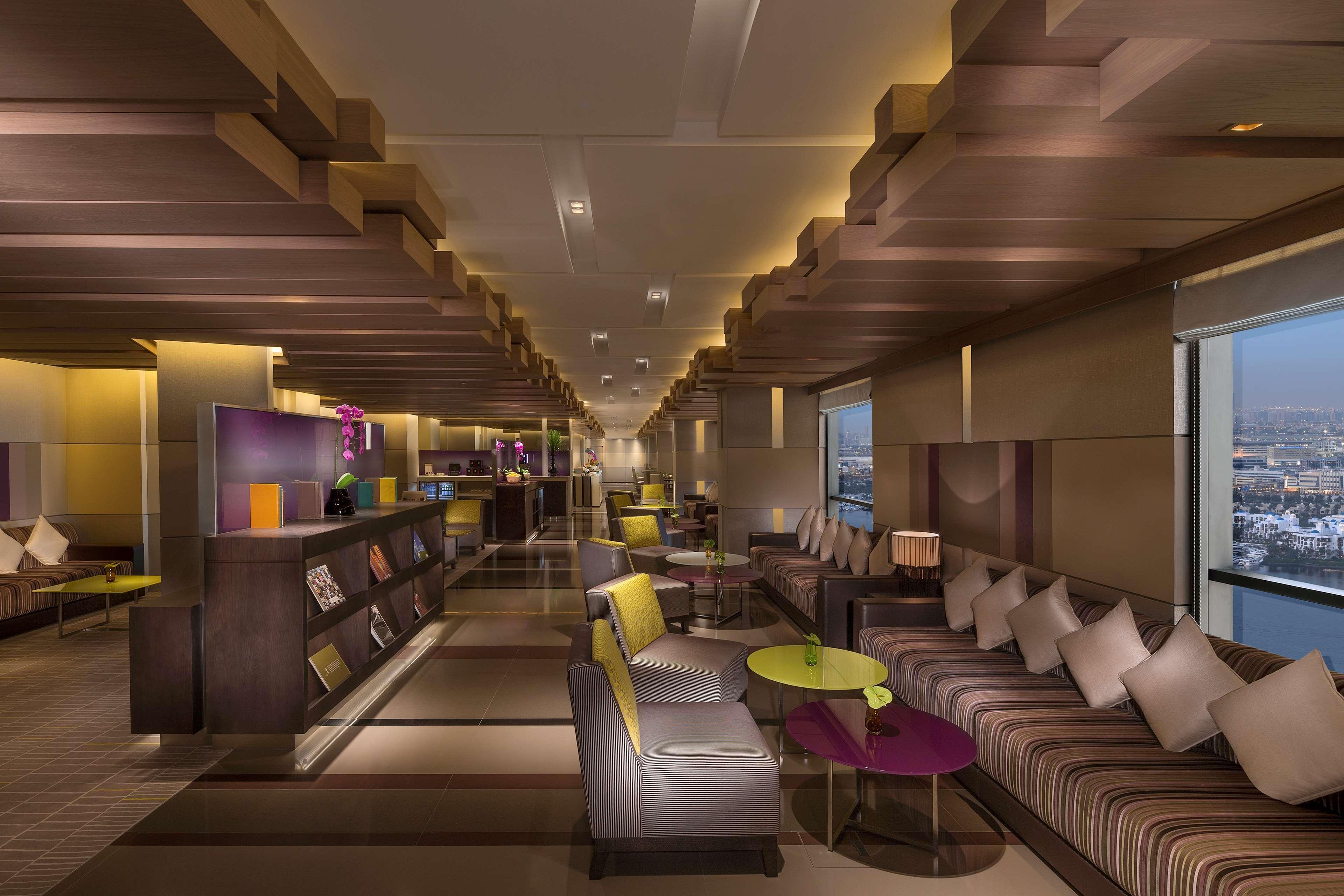 Hyatt Regency Dubai Creek Heights Hotel Exterior photo The photo showcases a modern and stylish interior of a lounge or café area. The space features a contemporary design with a warm color palette, including shades of yellow, purple, and brown. 

Comfortable seating is arranged throughout the area, with