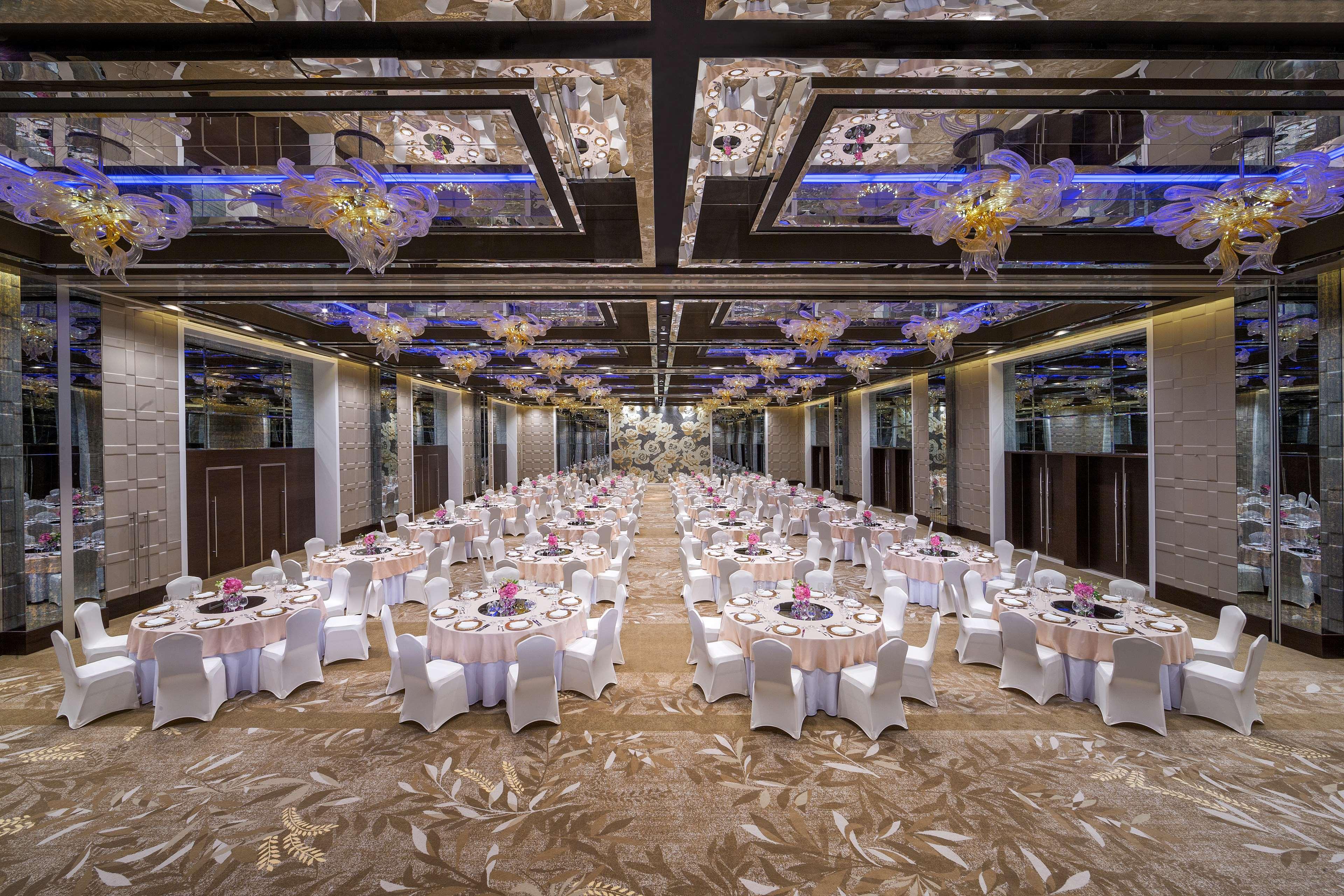 Hyatt Regency Dubai Creek Heights Hotel Exterior photo The photo shows a spacious banquet hall set up for an event. There are numerous round tables arranged in neat rows, each covered with white tablecloths. The tables are decorated with vases containing flowers and other centerpieces. The ceiling is ele