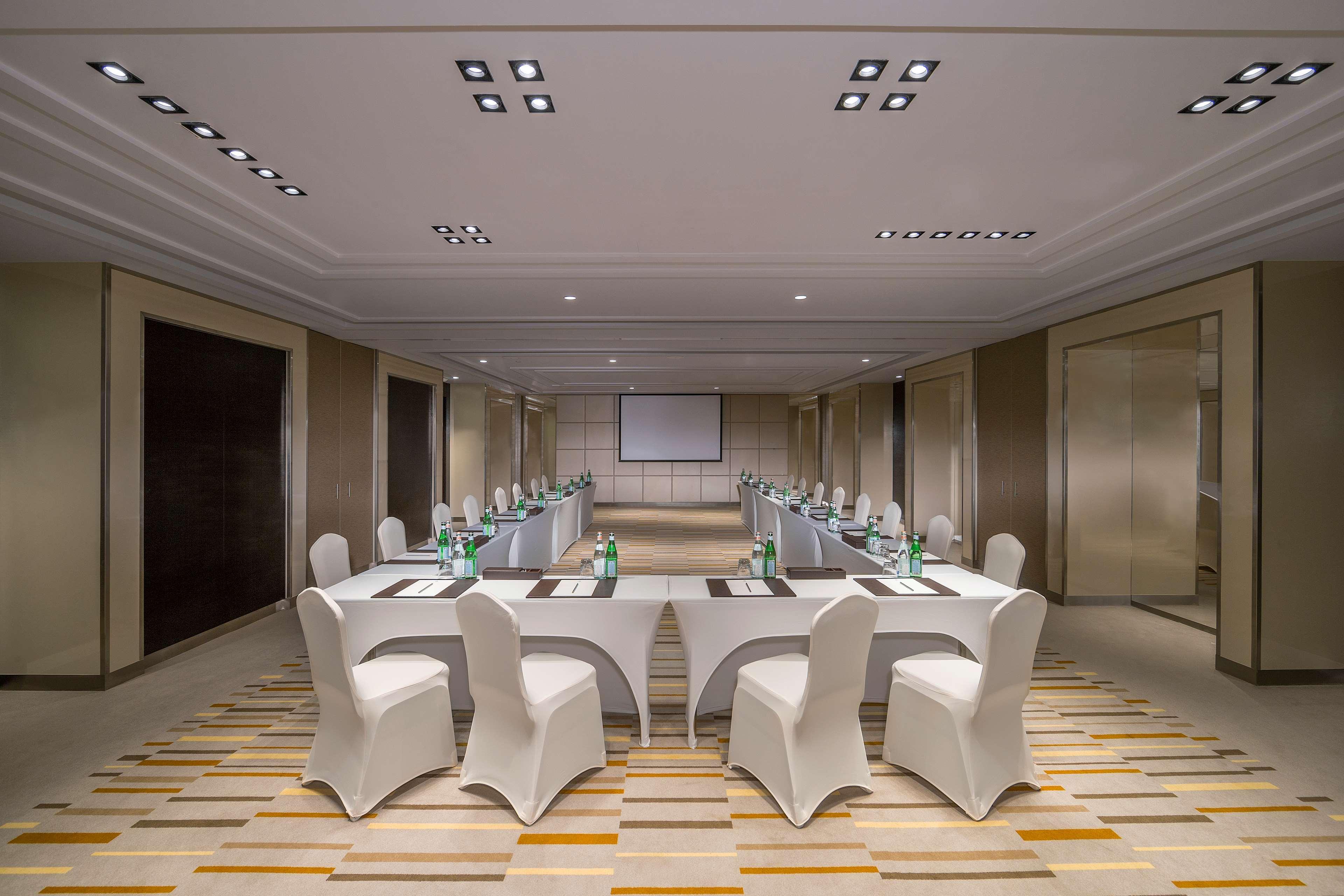 Hyatt Regency Dubai Creek Heights Hotel Exterior photo The photo shows a modern conference room set up for a meeting. There are several rectangular tables arranged in a U-shape, covered with tablecloths. Each table has water bottles and notepads placed on them, suggesting the presence of participants. Th