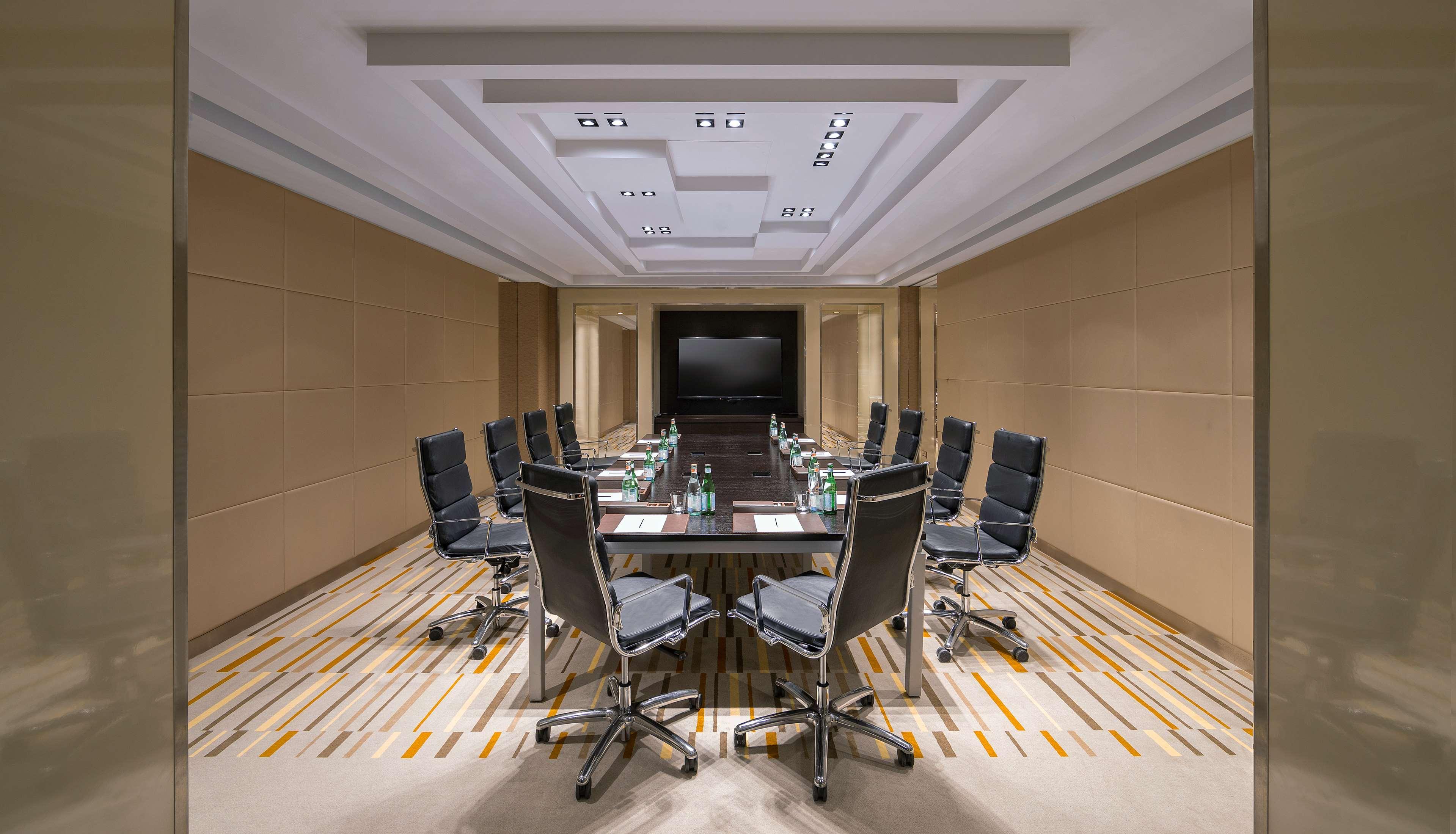 Hyatt Regency Dubai Creek Heights Hotel Exterior photo The photo shows a modern conference room set up for meetings. It features a large rectangular table surrounded by several ergonomic office chairs. The room has a neutral color scheme with beige walls and a patterned carpet. The ceiling is decorated w