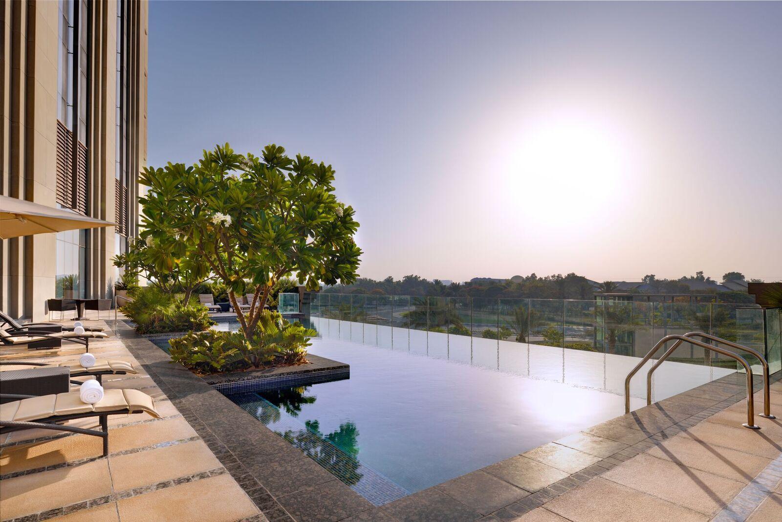 Hyatt Regency Dubai Creek Heights Hotel Exterior photo The photo depicts a luxurious outdoor swimming pool area. The pool features a sleek, modern design with an infinity edge that blends into the landscape. Surrounding the pool are comfortable lounge chairs and a small tree, adding a touch of greenery t