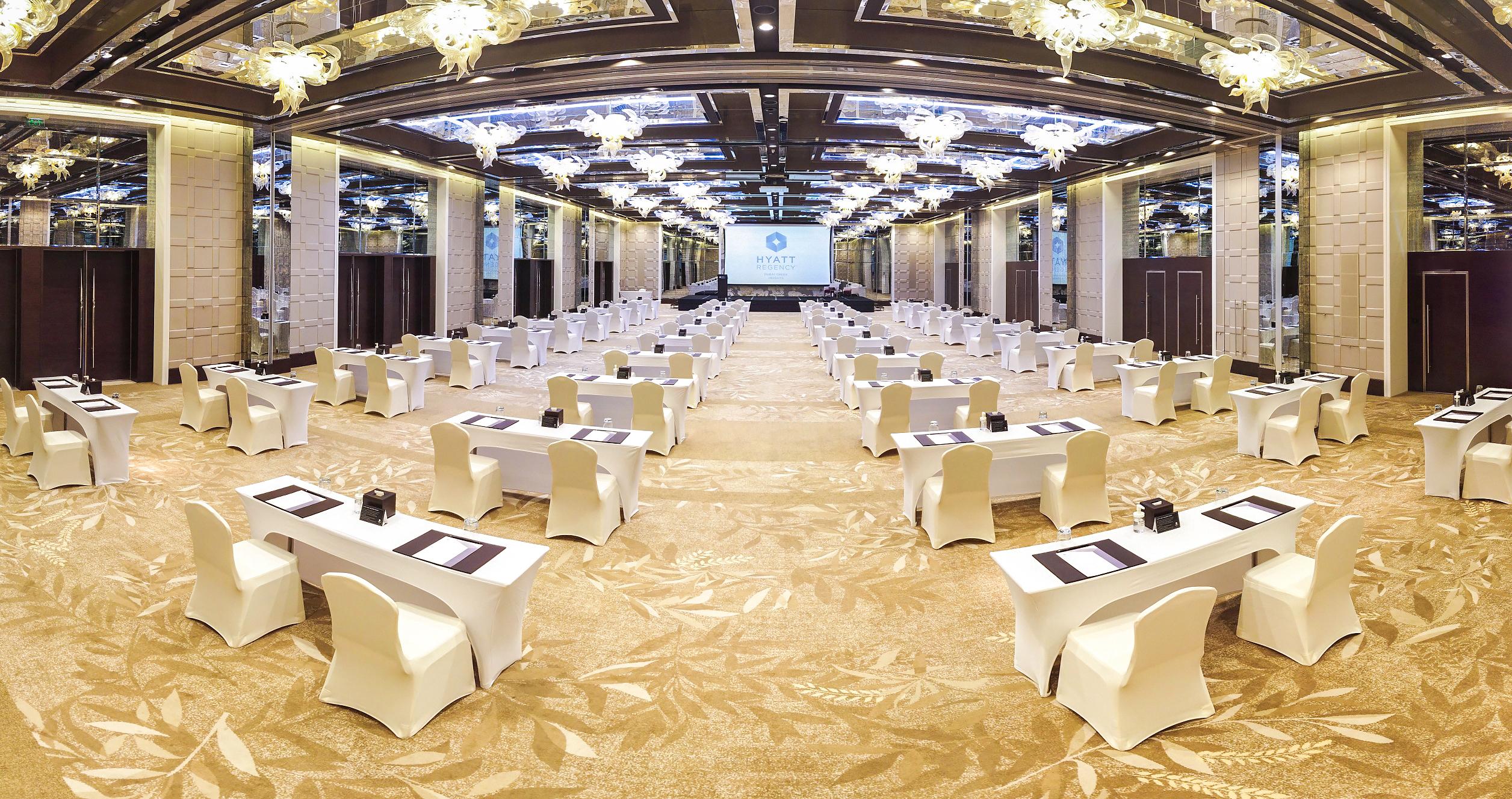 Hyatt Regency Dubai Creek Heights Hotel Exterior photo The image shows a large conference room set up for a meeting or event. There are multiple rows of tables arranged with white tablecloths and chairs, facing a screen at the front of the room. The ceiling features ornate chandeliers, and the floors hav