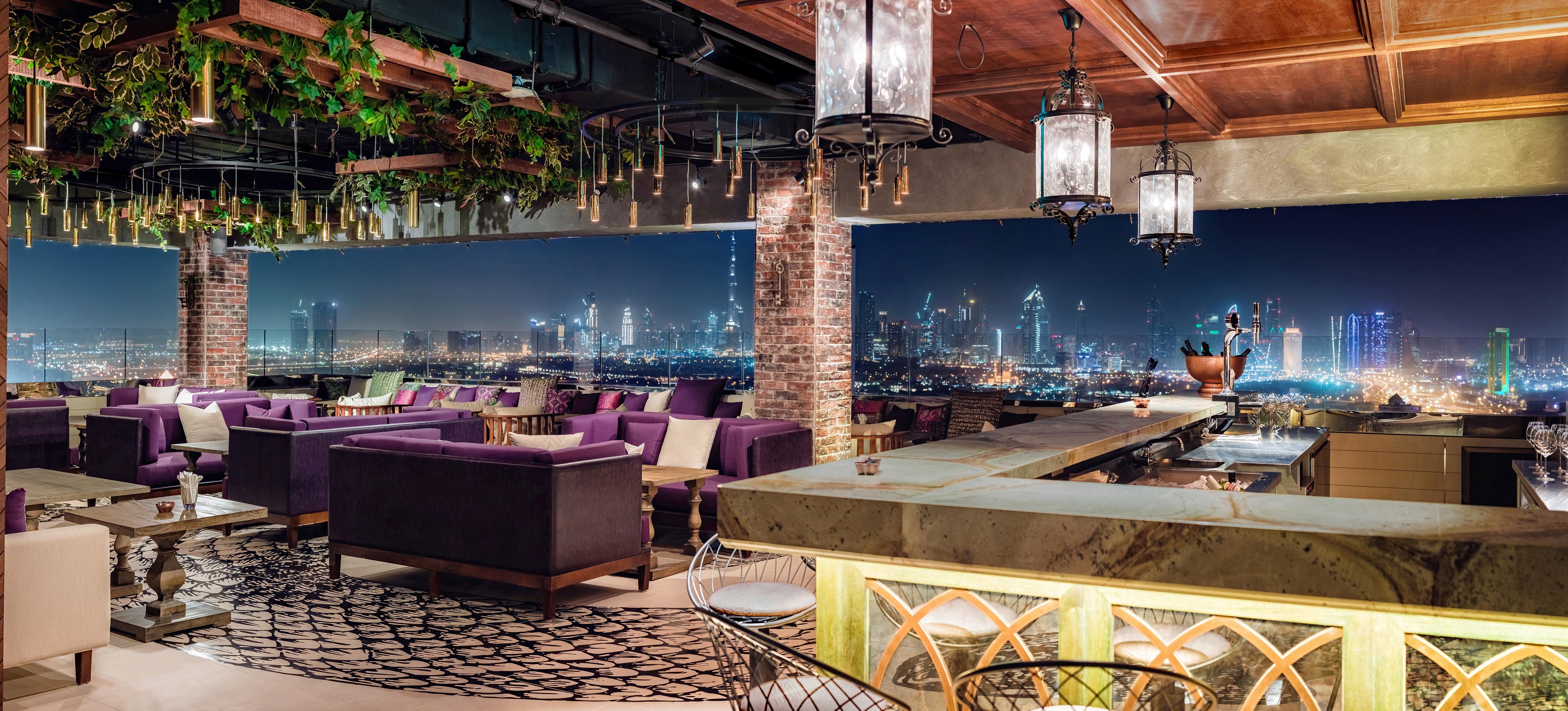 Hyatt Regency Dubai Creek Heights Hotel Exterior photo The photo depicts a stylish rooftop lounge or bar featuring a beautiful nighttime view of a city skyline. The interior design includes plush seating in shades of purple, creating a luxurious atmosphere. There are large windows that offer a panoramic 